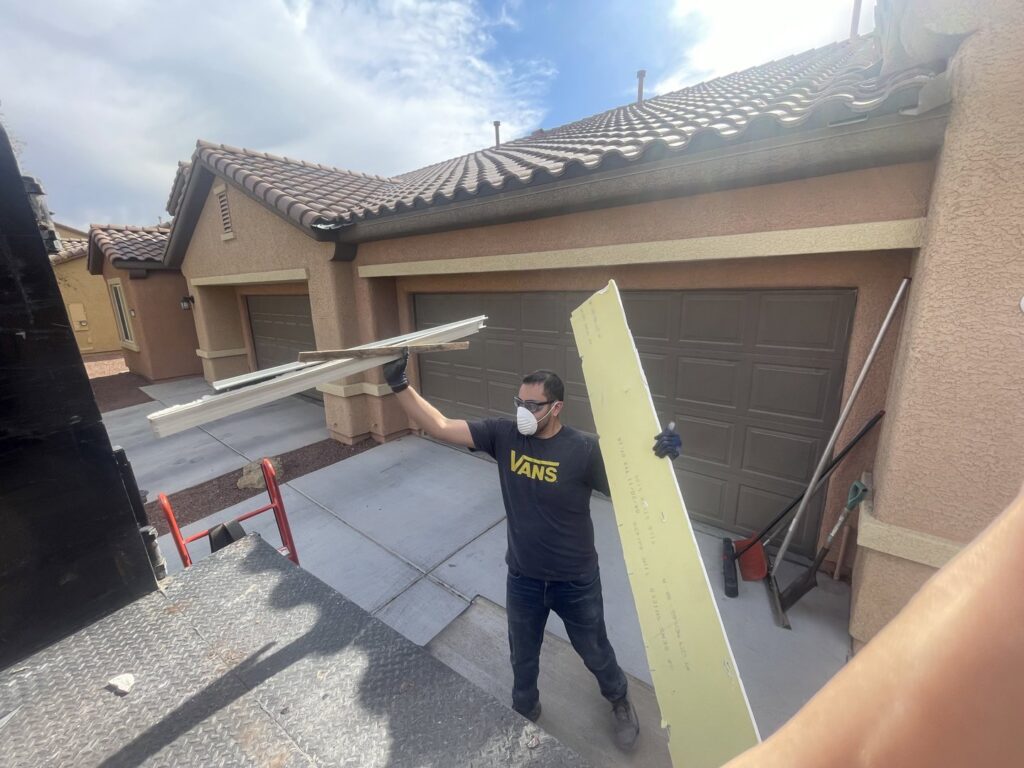 A Tidy Toss worker carrying long pieces of construction debris towards a junk removal truck in Las Vegas, NV