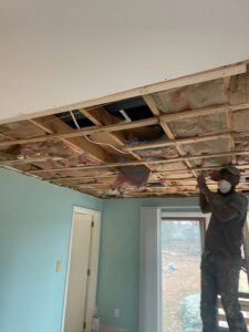 A worker on a ladder repairing a ceiling with exposed insulation, a service by Drywall Paint Plus in Worcester, MA.