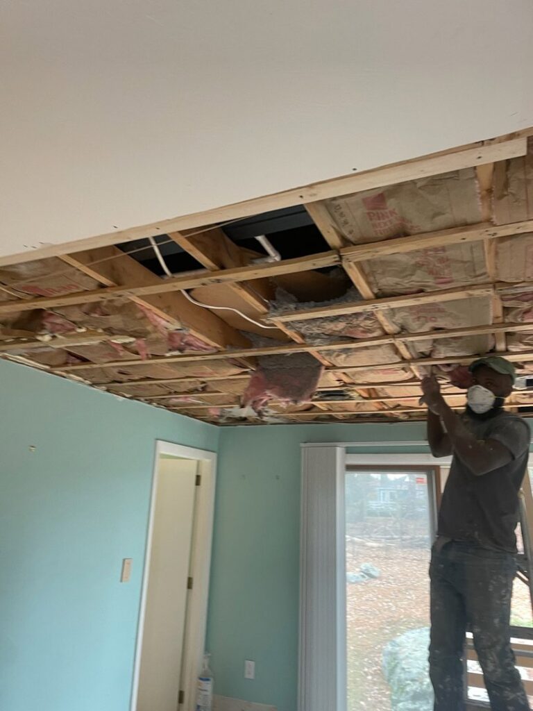 A worker on a ladder repairing a ceiling with exposed insulation, a service by Drywall Paint Plus in Worcester, MA.