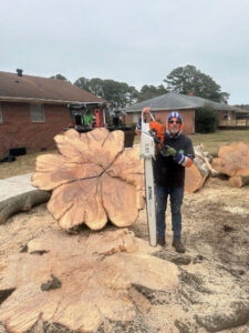 A tree service worker holding a large chainsaw next to a massive, decoratively cut tree stump by Scott Lanes Tree Service in Chesapeake, VA.