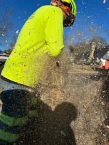 A worker in safety gear operating a chainsaw, cutting wood with chips flying, for Ratliff Landscape and Tree Service LLC in Murfreesboro, TN