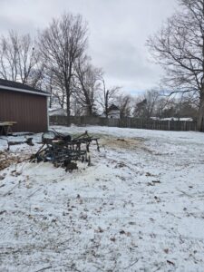 A tree service worker cutting logs with a chainsaw behind a fence for Father and Son Tree Service in Lansing, MI.