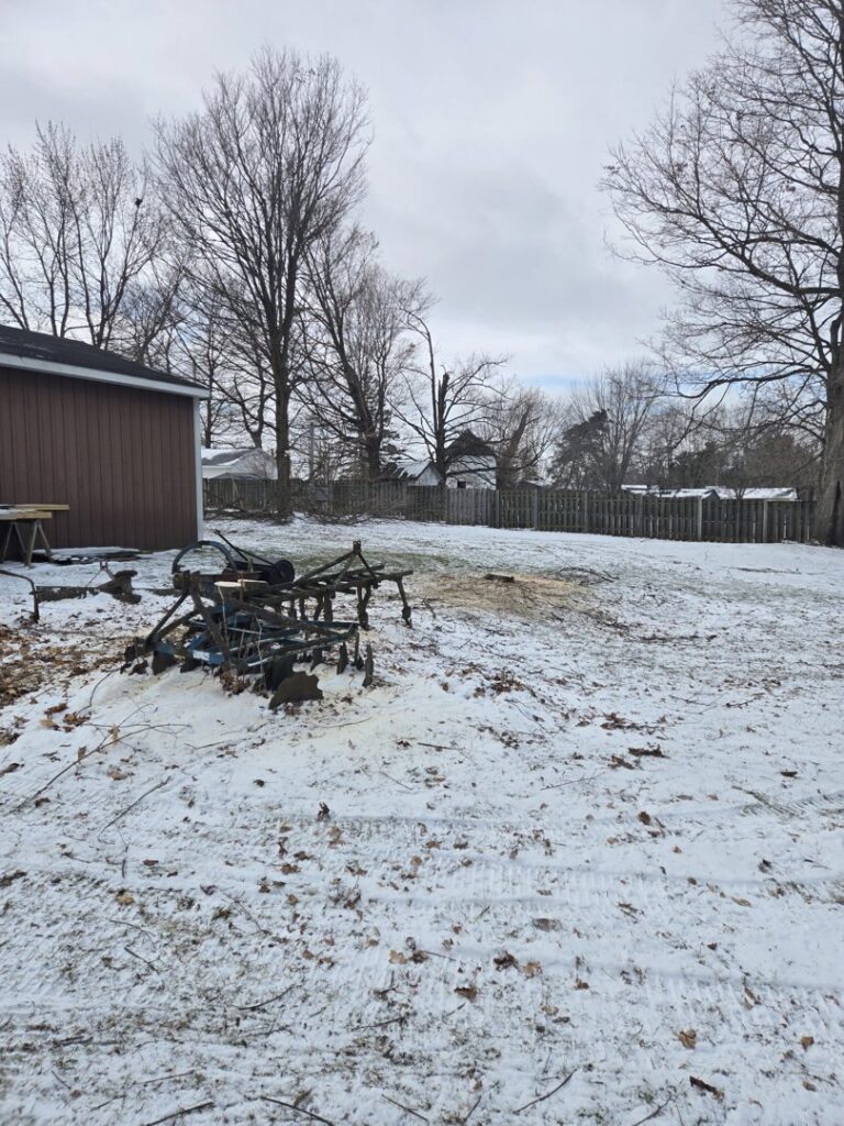 A tree service worker cutting logs with a chainsaw behind a fence for Father and Son Tree Service in Lansing, MI.