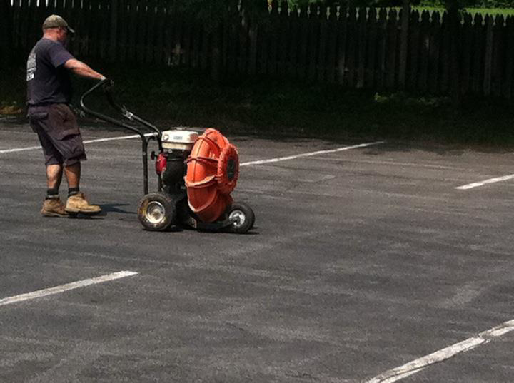 A worker using a leaf blower to clear a parking lot before sealcoating by Empire Sealcoating in Albany, NY
