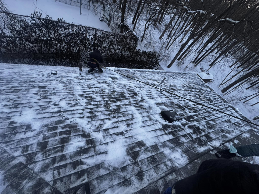 A worker clearing snow from a residential roof, providing handyman services by BETHO Construction INC in Milford, MA.