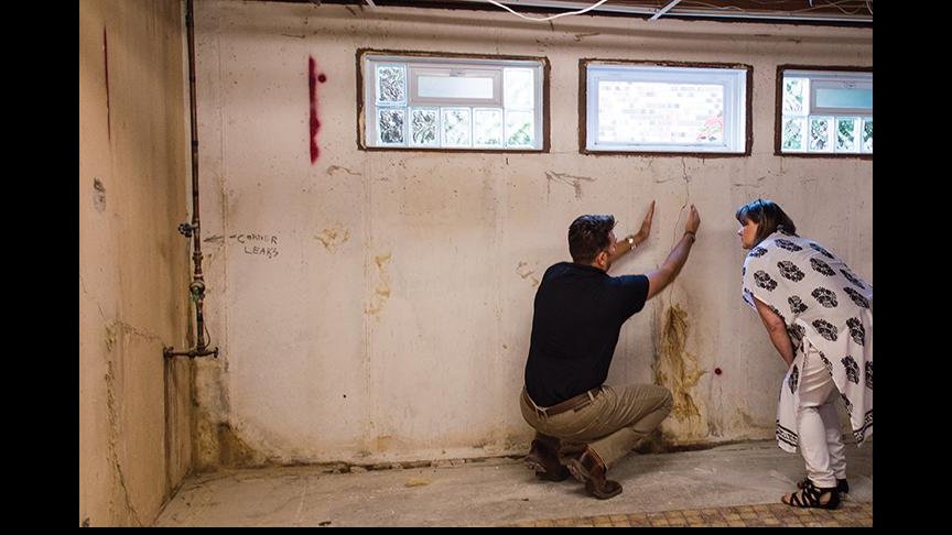A Helitech Waterproofing & Foundation Repair worker and a client inspecting cracks and water damage on a basement wall in Kingdom City, MO.