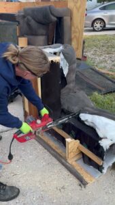 Worker using chainsaw to cut up large upholstered furniture during junk removal by Tiny Monster Junk Removal LLC, Denver, CO.