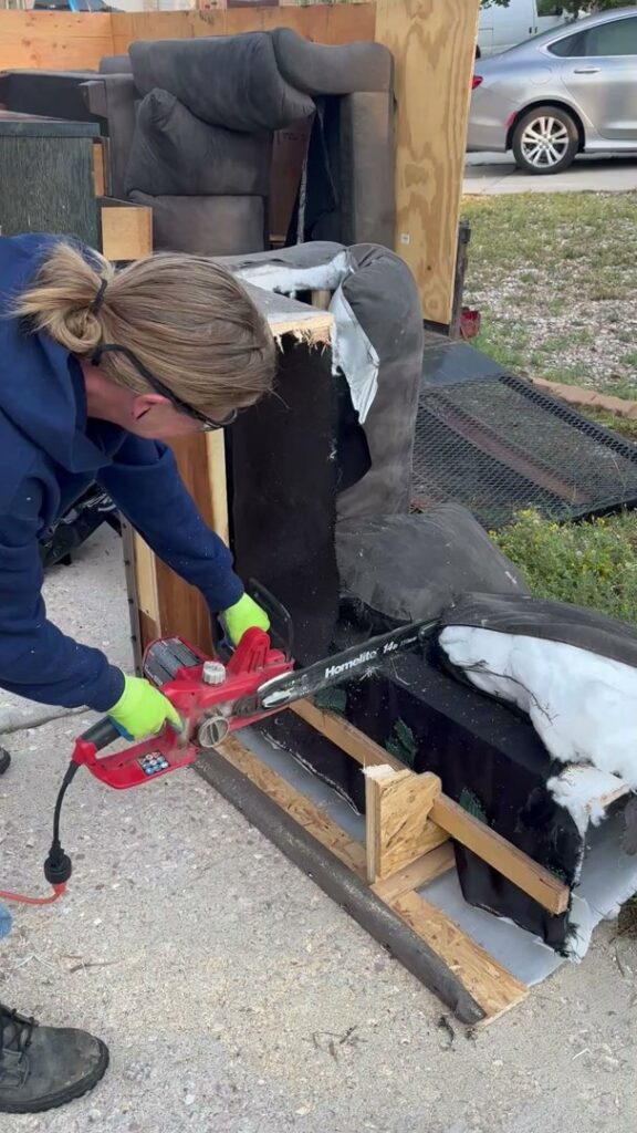 Worker using chainsaw to cut up large upholstered furniture during junk removal by Tiny Monster Junk Removal LLC, Denver, CO.