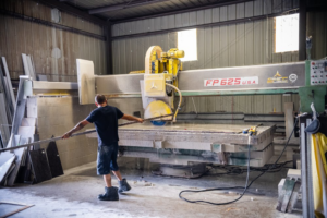 A worker cutting a large granite slab with a saw machine at L&M Granite Countertops in Phoenix, AZ.