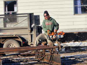A worker cutting scrap metal with a large saw, performing junk removal services for 701 Scrap in Williston, ND.