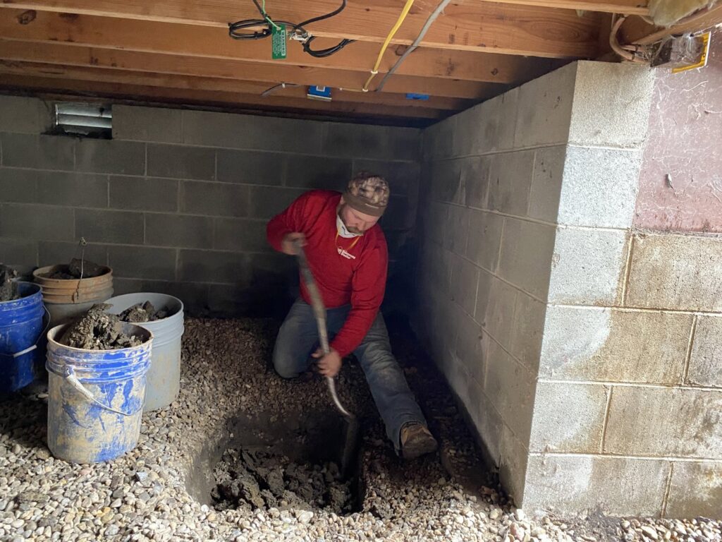 A worker digging a trench for drainage in a basement by The Basement Doctor in Reynoldsburg, OH.