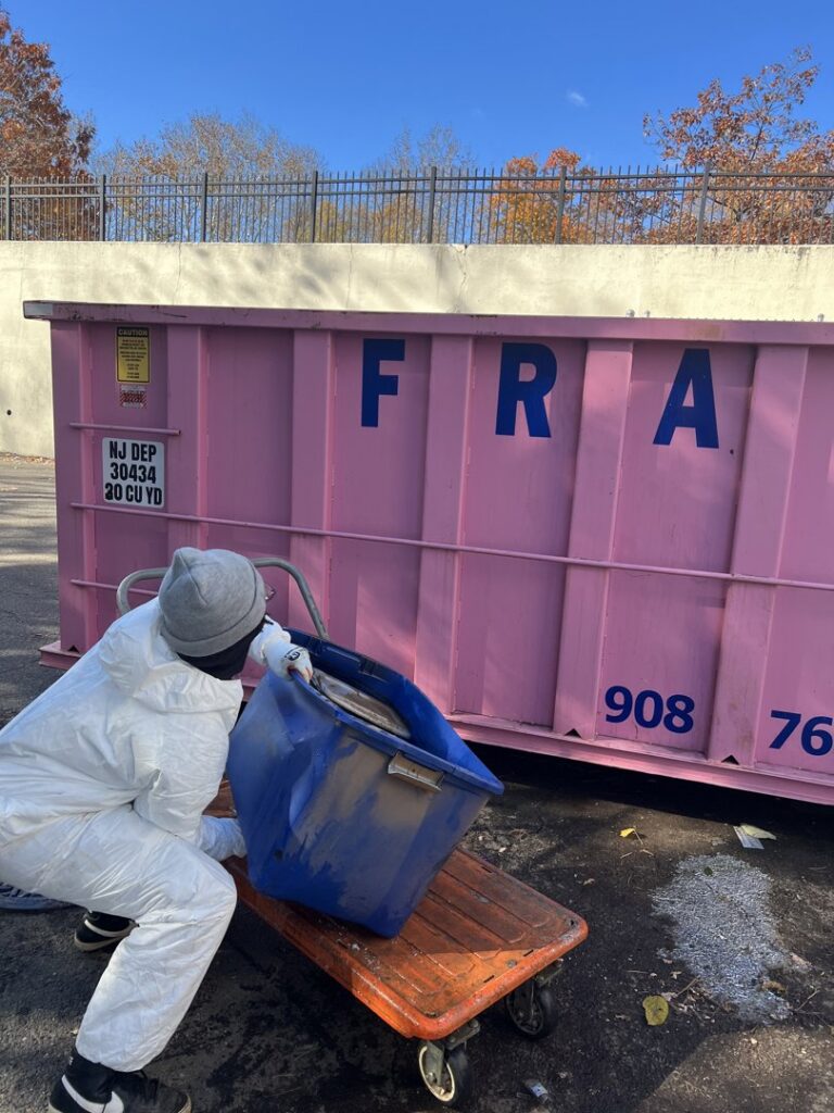 A worker in a protective suit disposing of debris into a large dumpster for Professional Restoration in Jersey City, NJ
