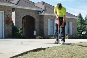 A Helitech Waterproofing & Foundation Repair worker drilling into a concrete driveway for leveling in Kingdom City, MO.
