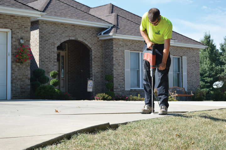A Helitech Waterproofing & Foundation Repair worker drilling into a concrete driveway for leveling in Kingdom City, MO.