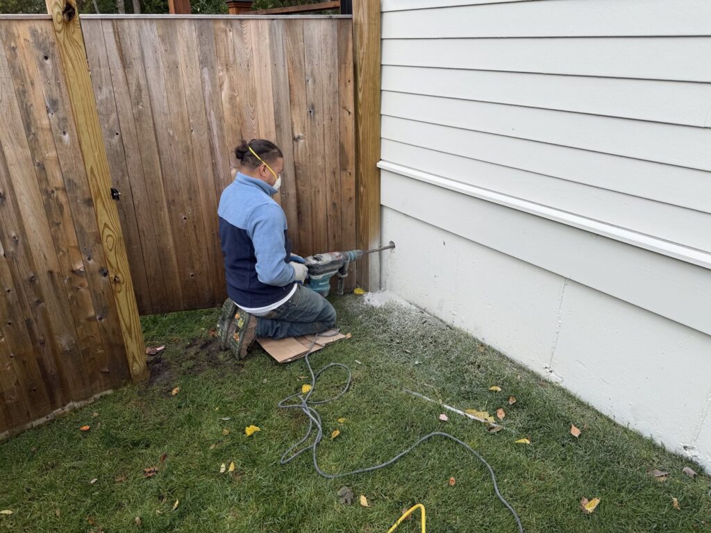 A worker from B-Dry System of New England drilling into an exterior house wall for a waterproofing installation in North Billerica, MA.
