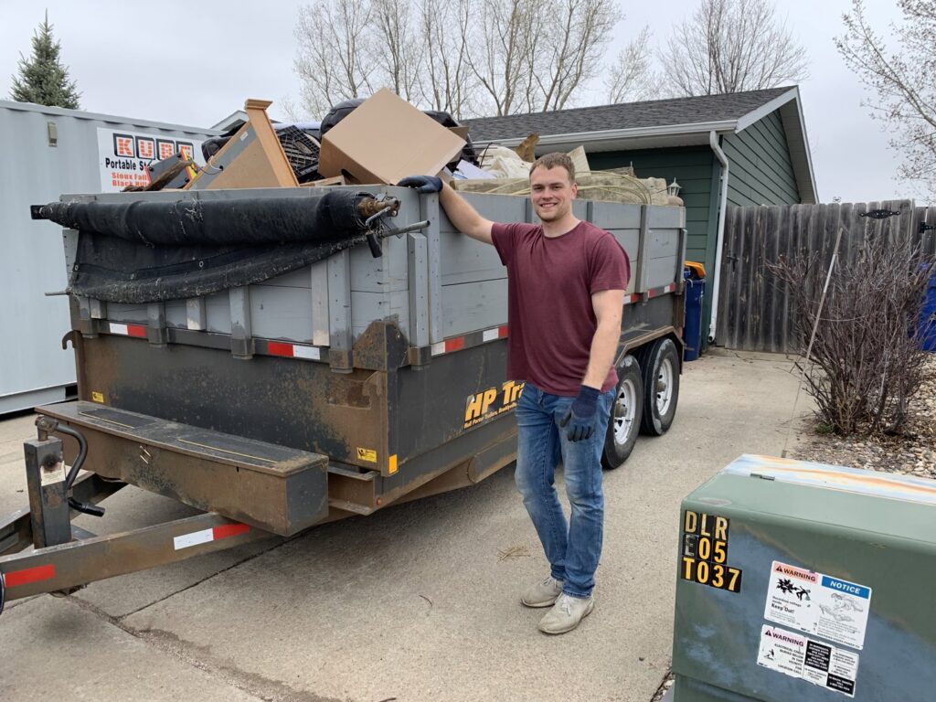 A WeHaul Hauling & Junk Removal team member standing next to a dump trailer filled with junk in Sioux Falls, SD.