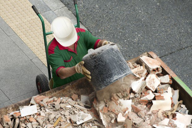 A worker emptying a bucket of construction debris into a roll-off dumpster for junk removal in Sterling Heights, MI.