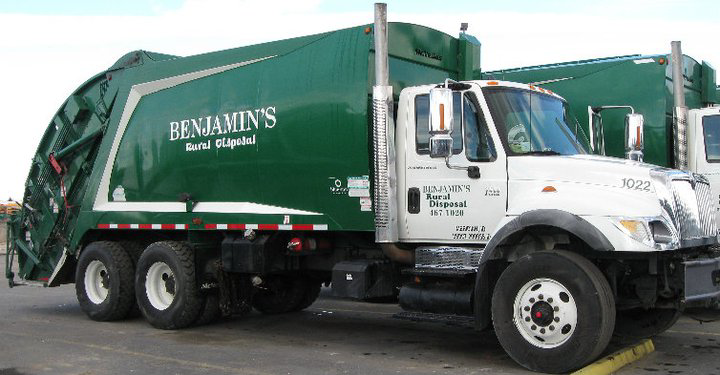 A worker in a high-visibility vest emptying a residential garbage bin into a Benjamin's Rural Disposal truck in Meridian, ID.