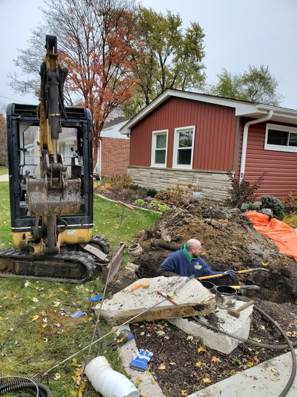 A worker excavating a plumbing line with an excavator at a job site for Hessville Plumbing in Hammond, IN.