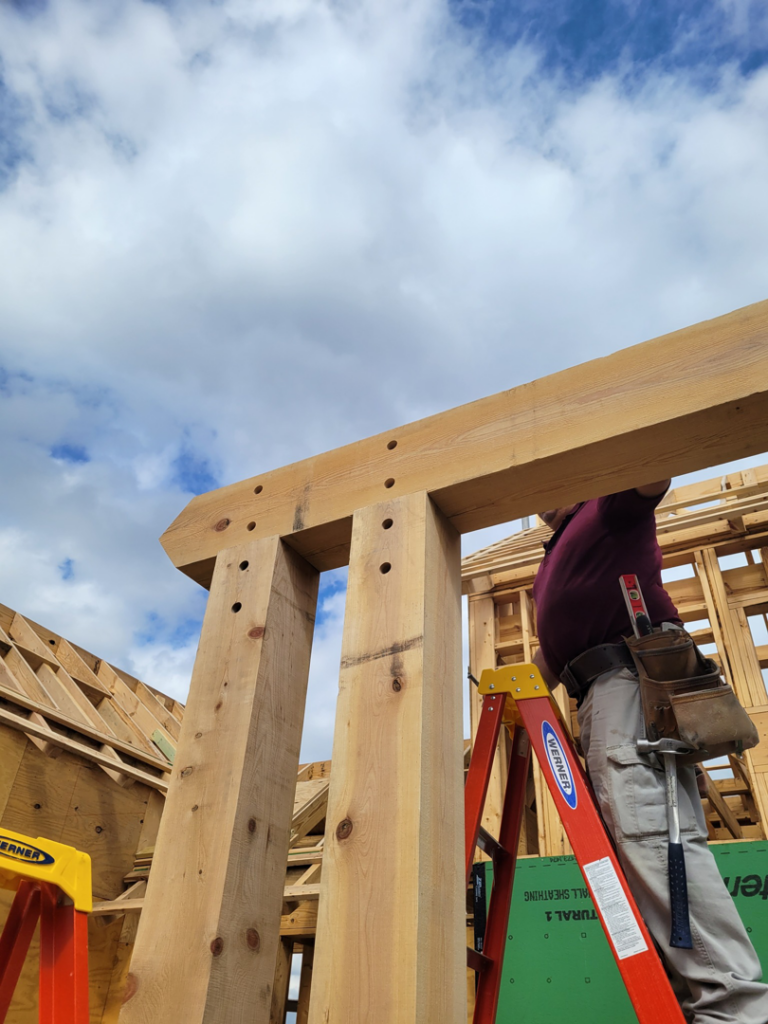 A construction worker on a ladder framing a large timber structure at a job site by Hill Country Framing in Austin, TX