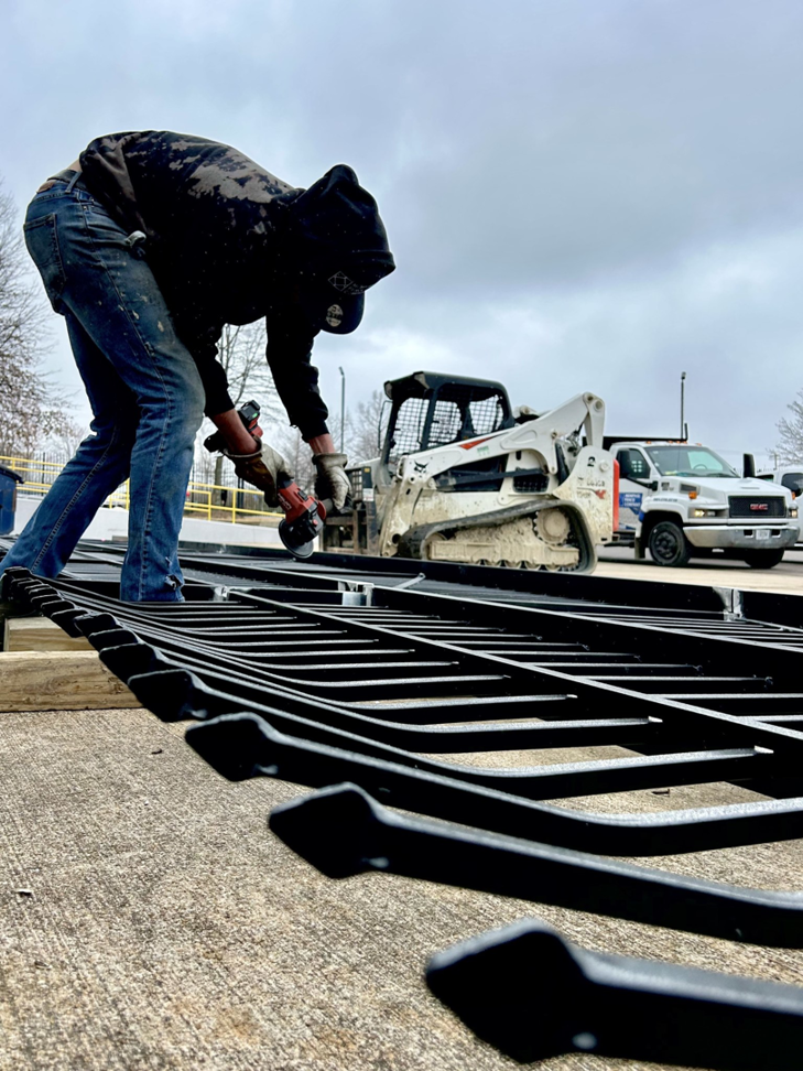 A worker using an angle grinder to modify a metal fence panel, a handyman service from Memphis Fence Company, LLC in Memphis, TN.