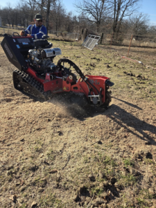 A skilled worker actively grinding a tree stump with a professional stump grinder, demonstrating work by Garcia's Tree service in Louisville, KY.
