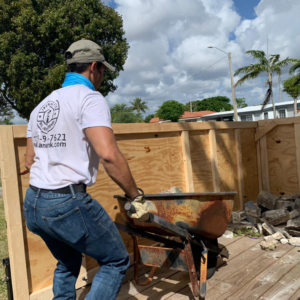 A worker hauling construction debris in a wheelbarrow towards a trailer for Jays Haul and Junk in Miami, FL.