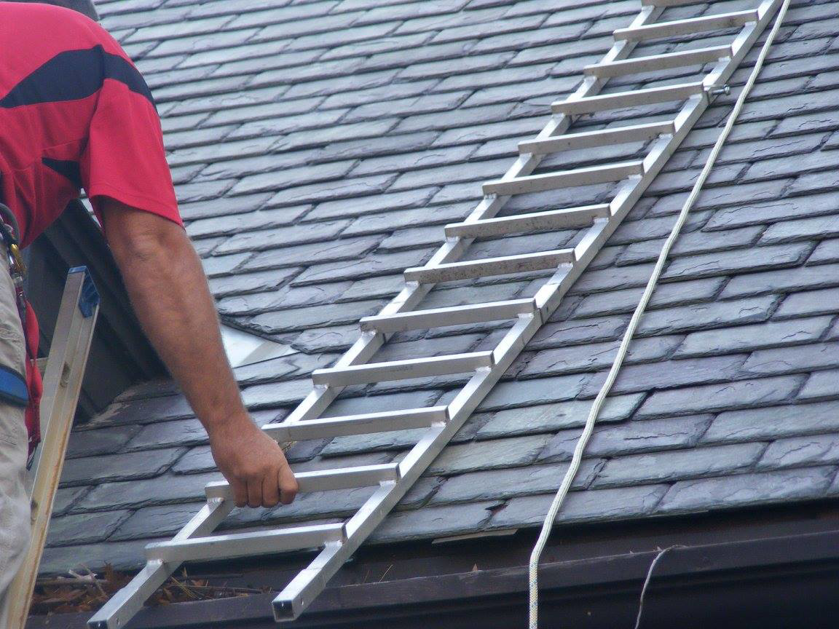 A worker holding onto a roof ladder on a slate roof, demonstrating work by Superior Roof Support in Milano, TX.