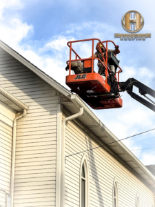 A Henderson Roofing handyman in Canton, OH, working from a boom lift to repair gutters on a building.