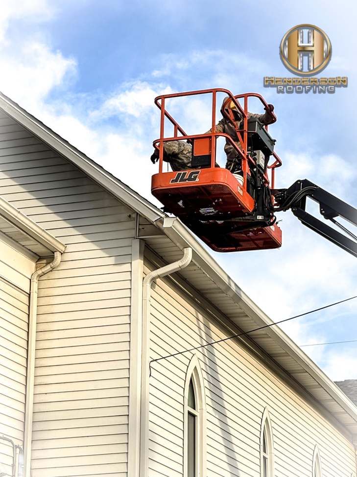A Henderson Roofing handyman in Canton, OH, working from a boom lift to repair gutters on a building.