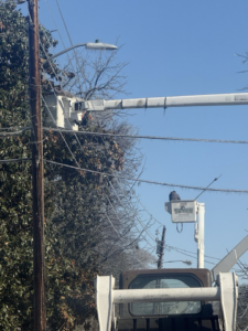 A worker in a Toten Tree Service bucket truck clearing ice from trees and power lines in Greenville, MS.