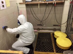 A worker in a hazmat suit cleaning hazardous residue from a wall, demonstrating environmental services by MLi Environmental in South Portland, ME.