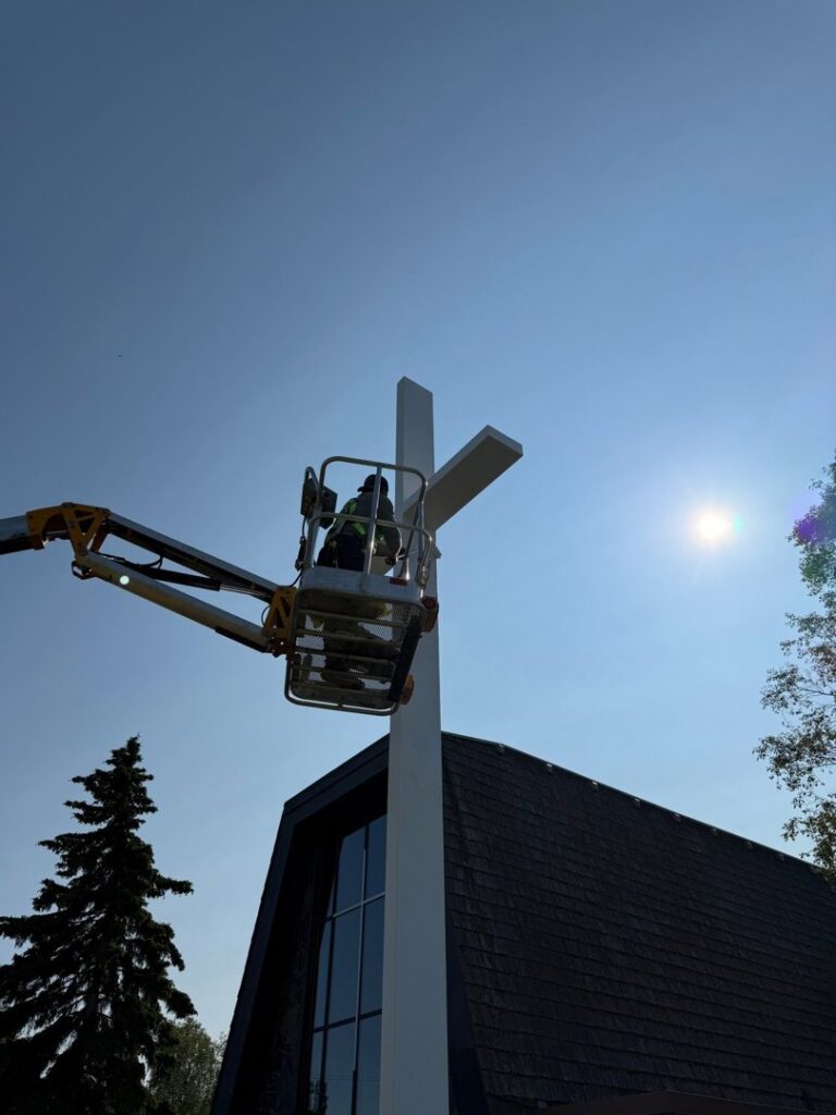 A worker in a lift installing a large white cross structure for Alaskan Residential Rescue in Anchorage, AK.