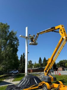 A worker in a lift painting a large white cross structure, a service provided by Alaskan Residential Rescue in Anchorage, AK.
