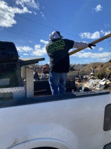 A Goblins Junk Removal worker in a pickup truck bed, pointing towards a large pile of debris at a job site in Wheat Ridge, CO.