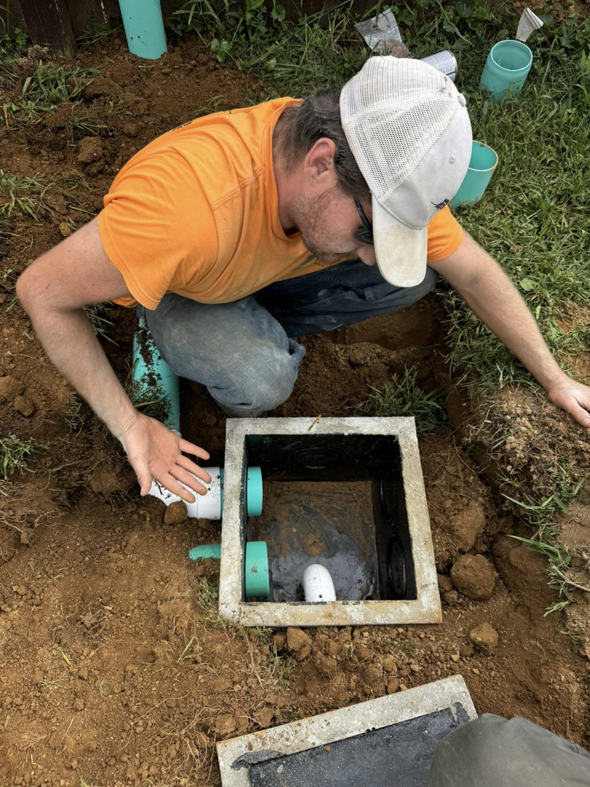 A worker inspecting a concrete drainage system box with pipes, a handyman service by Richardson Ridge Construction in Bloomington, IN.