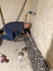 A worker from B-Dry System of New England installing drainage pipes and gravel for a basement waterproofing system in North Billerica, MA.