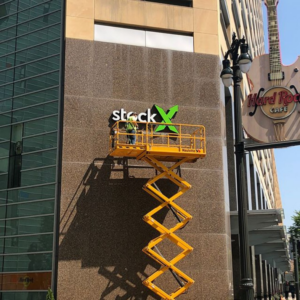 A worker on a scissor lift installing a commercial sign on a building for DKI Demolition in West Bloomfield Township, MI.