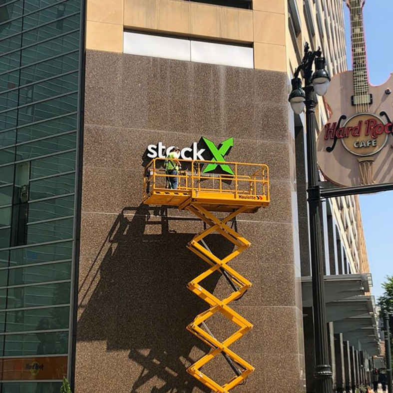 A worker on a scissor lift installing a commercial sign on a building for DKI Demolition in West Bloomfield Township, MI.