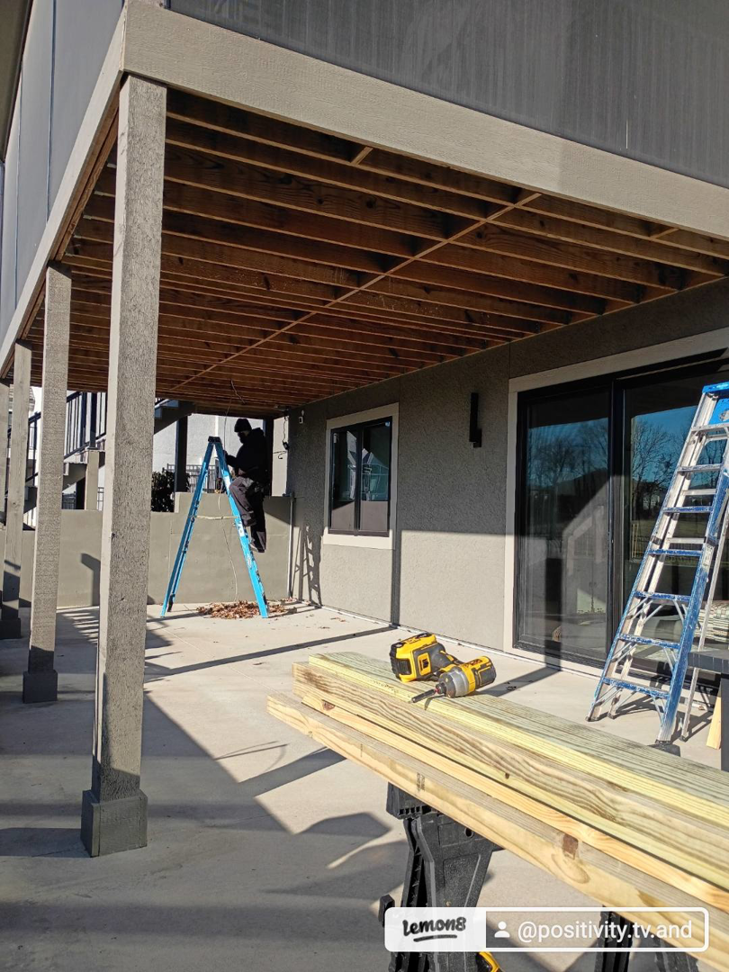 A worker on a ladder installing a new deck ceiling with lumber and tools on site by Dry Deck Ceilings KC in Kansas City, KS.