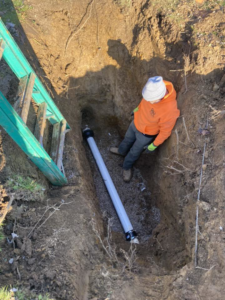 A worker installing a large drainage pipe in a deep trench, a service offered by Richardson Ridge Construction in Bloomington, IN.