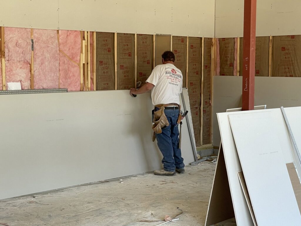 A worker installing a large sheet of drywall onto a framed wall for Hahn Brothers Drywall Co Inc in Evansville, IN