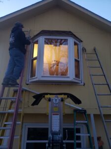 A worker on a ladder installing an exterior bay window on a house for Rosewalls Handyman & Remodeling in Des Moines, IA.