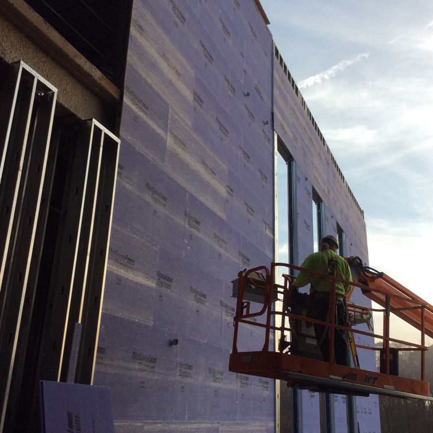 A worker on a lift installing exterior sheathing on a commercial building for Combs Interior Specialties in Columbus, OH.