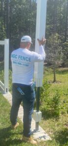 A worker from NGC FENCE INC installing a white vinyl fence post in Jacksonville, FL.