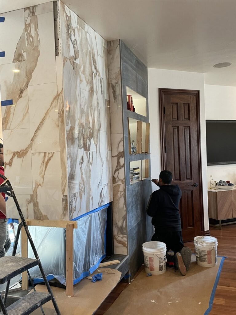 A worker installing large format marble tiles on a fireplace surround at a home in Lakewood, CO by The Foundation Guys