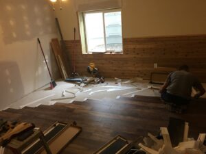 A worker installing new flooring and wood wall panels in a room, demonstrating interior handyman services by Advanced Construction of Janesville LLC in Janesville, WI.
