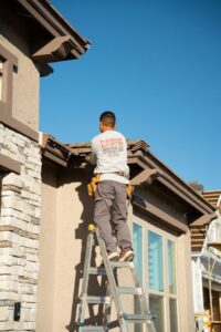 A worker from Phoenix Rain Gutters and Sun Protection on a ladder installing or maintaining gutters on a house in Glendale, AZ.