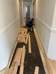 A worker installing hardwood flooring planks in a hallway by Just Floor It Hardwood Floors LLC in Philadelphia, PA