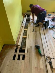 A worker installing hardwood flooring, with subfloor exposed and tools nearby, by NV Floors LLC in Pittsburgh, PA.